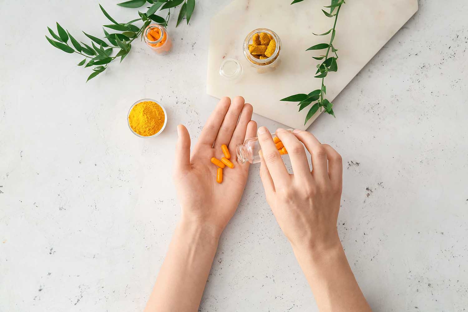 Female hands with turmeric pills, powder and roots on light background