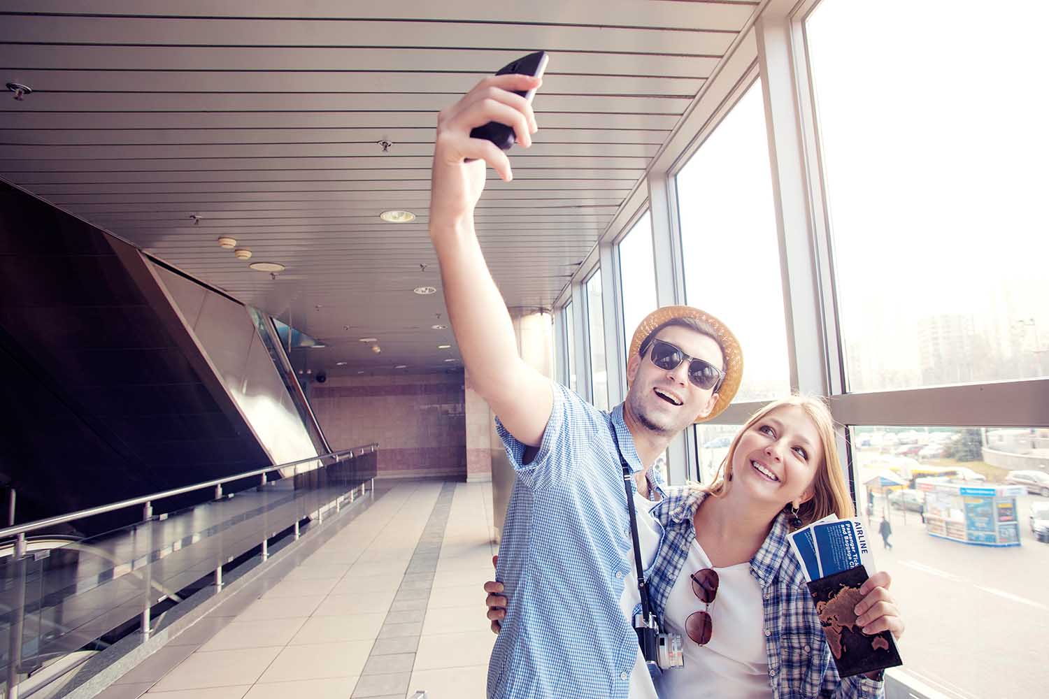 We love traveling! Vacation Selfie. Beautiful young loving couple making selfie by their smart phone while waiting for boarding in the airport.