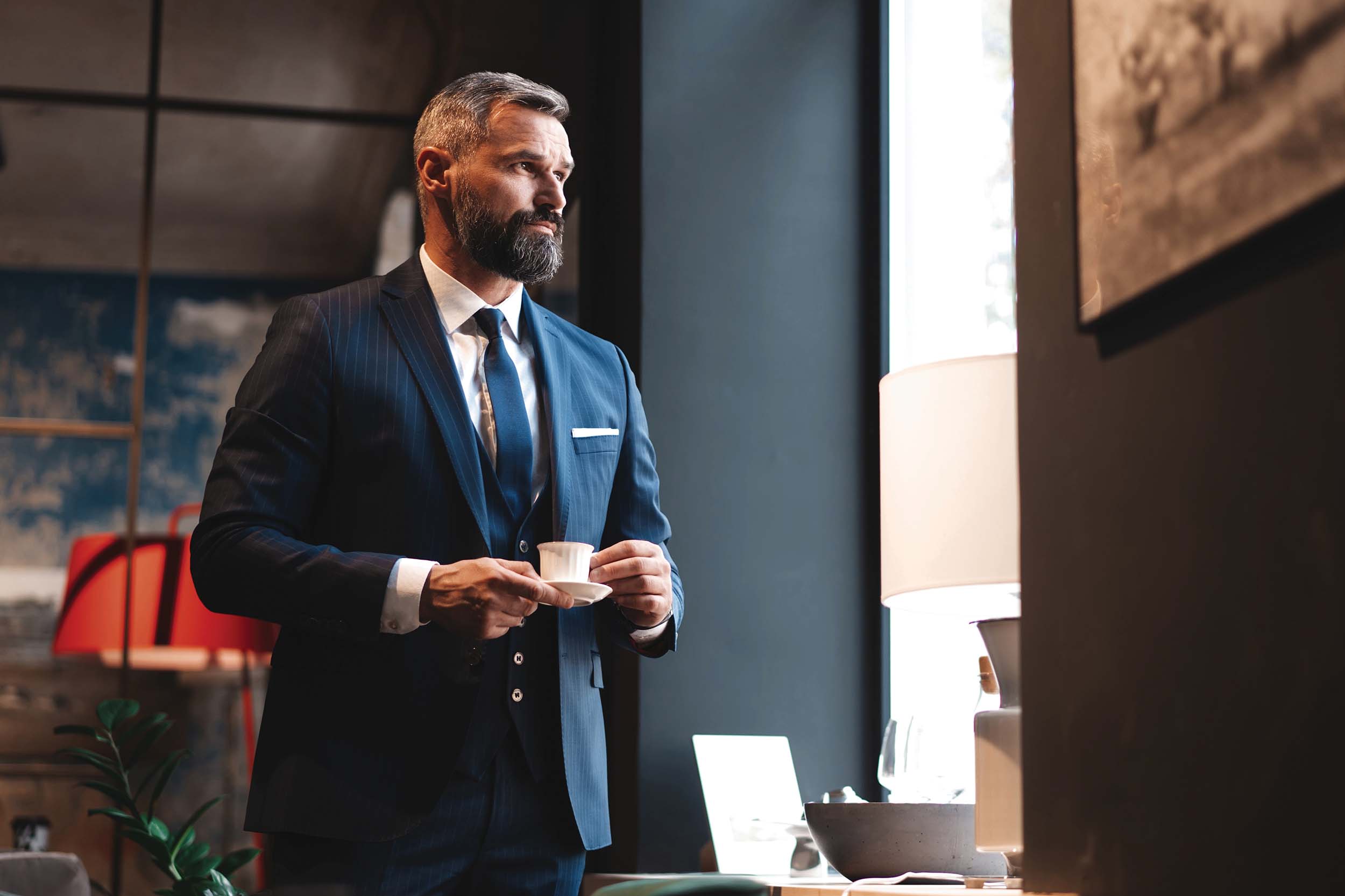 Enjoying fresh coffee while working. Confident man in smart casual wear holding coffee cup at his working place in office