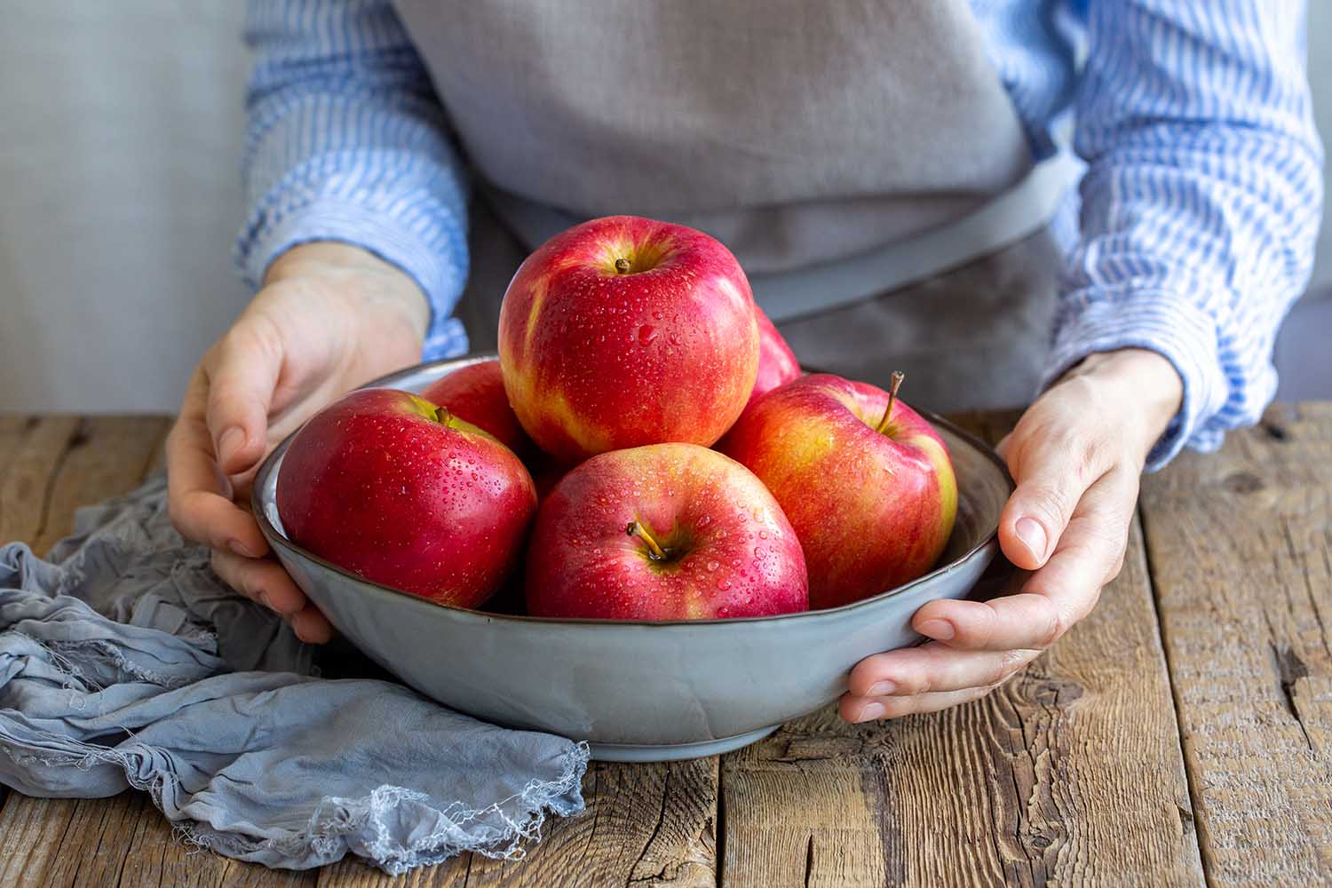 Apple saved. Apples washed in a bowl in the hands of the girl. A plate with red apples on a wooden table. Cooking food. Vegan. Food for vegetarians and vegans. Fresh fruits. Vitamins. Proper nutrition